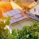 Solar panels on the tiled roof of the building in the sun. Top view through grape leaves. Selective focus. stock photo